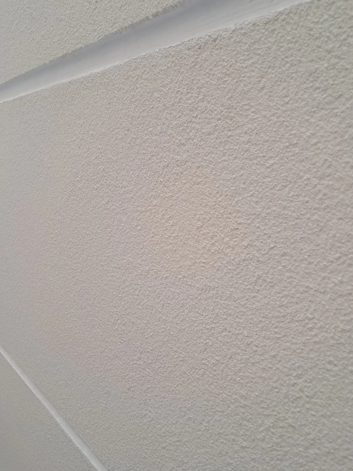 Close de parede em arenato branco, com o grão fino aparente e frisos finos cruzando o pano